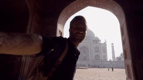 Tourist male taking selfie at the famous Taj Mahal at sunset using mobile phone, Agra, India. People travel Asia concept - Young man having fun discovering India 