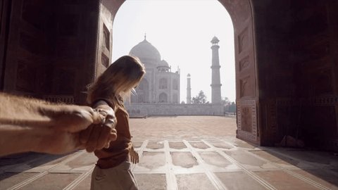 Follow me to the Taj Mahal, India. Female tourist leading way to boyfriend to magnificent famous Mausoleum in Agra. People travel concept - Girl holding man hand at sunrise traveling together- Slow mo