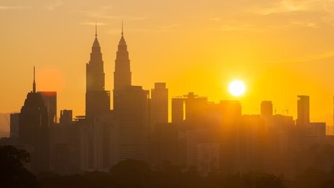 Time lapse: Silhouette of KL cityscape view during golden dawn overlooking the city skyline from afar with yolk sun and lushes green in the foreground. Kuala Lumpur, Malaysia.  Zoom out motion.