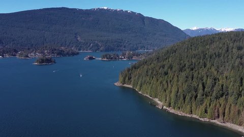 Aerial view over Burrard Inlet, ocean and island with old pier and mountains in beautiful British Columbia. Canada. 4K.