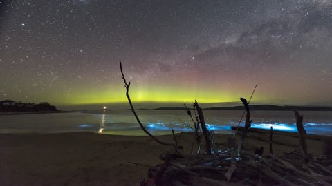 Time lapse of the Aurora Australis or Southern Lights over a beach in Tasmania with spectacular neon blue bioluminescence in the waves breaking on the beach.