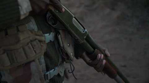 Close up following shot of an anti-poaching camouflaged ranger's gun as he walks into the early morning sunlight