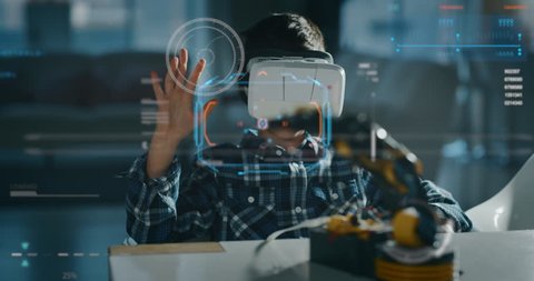 Portrait of boy playing with mechanical arm toy using vr glasses with futuristic augmented reality hologram in living room in slow motion.
