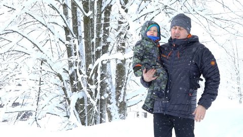 Man carrying his son in the snow covered winter forest, slow motion