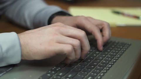 A video of a man typing in his office at his nice wood desk. 120 FPS slow motion.