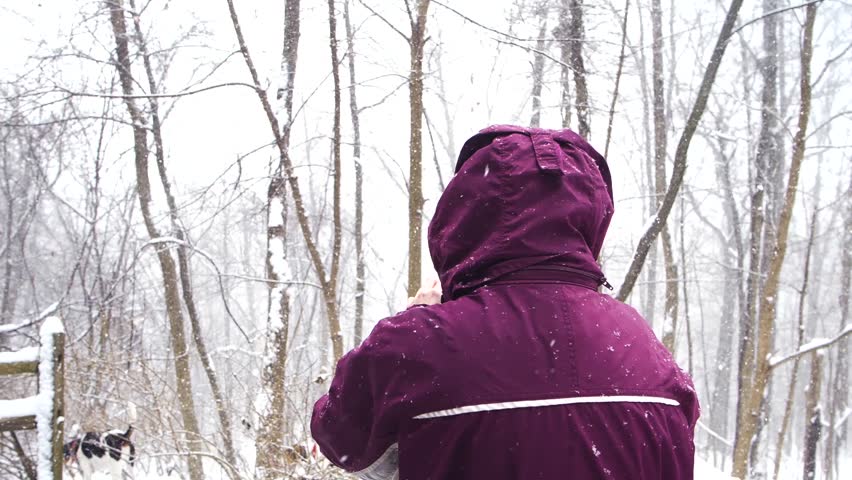 Woman filming outdoors with a cellphone in the snow during a snowstorm wearing a heavy coat.