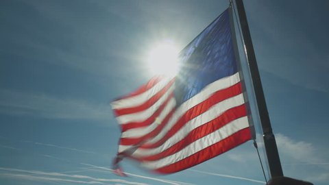 United States flag flapping powerfully in the wind as the sun creates a flare behind it Video stock