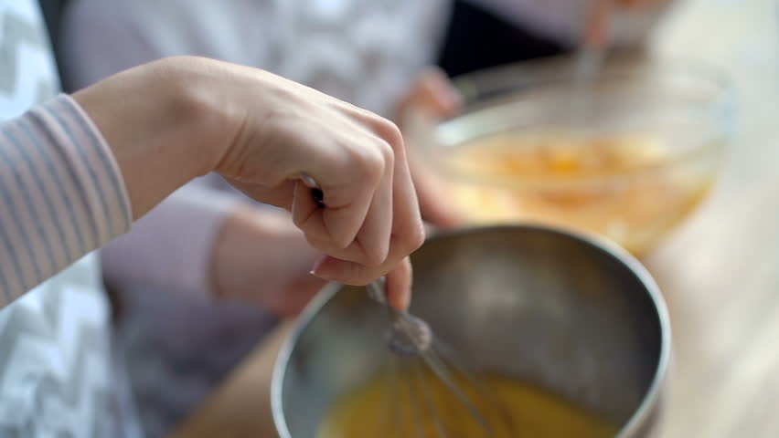 Close up. Mother daughter cooking together. Kid girl mixing dough in the bowl. Focus on the female hand, than on the kid girl face. Royalty-Free Stock Footage #1026776306