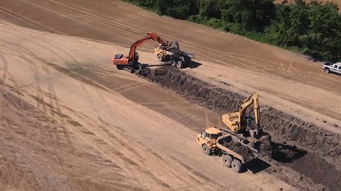Aerial of two excavators working simultaneously digging up dirt and loaded into dump trucks.