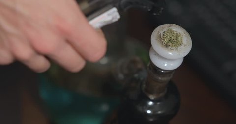 Medical marijuana is lit and inhaled from a bong and cannabis smoke slowly falls.