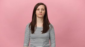 Smiling mystery brunette young woman in striped shirt looking aside, at camera, eavesdropping interesting news isolated over pastel pink background in studio. People sincere emotions lifestyle concept