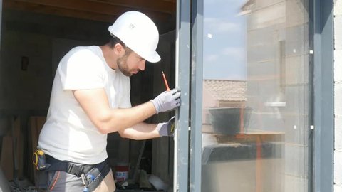 handsome young man installing bay window in a new house construction site
