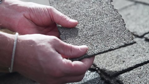 Roof inspector cracking old asphalt shingles during residential inspection