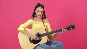studio shoot of happy young woman playing acoustic guitar isolated on crimson