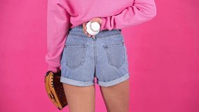cropped view of woman in denim shorts and with baseball glove holding ball behind back isolated on crimson