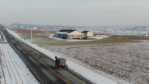 Amish buggy with horse driving over empty road in rural area. Shot in Intercourse, PA in winter. A beautiful snow covered rural town with farms, meadows, farmlands and a small village center.