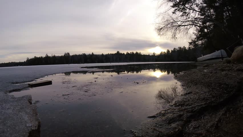 Beautiful sunset time lapse from icy lake winnipesaukee in New Hampshire. Bright sky and clouds above natural beach and froze lake water.