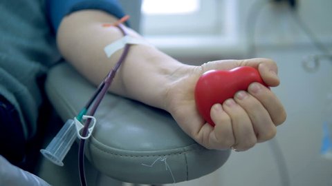 A person squeezes a ball while donating blood at a transfusion center.