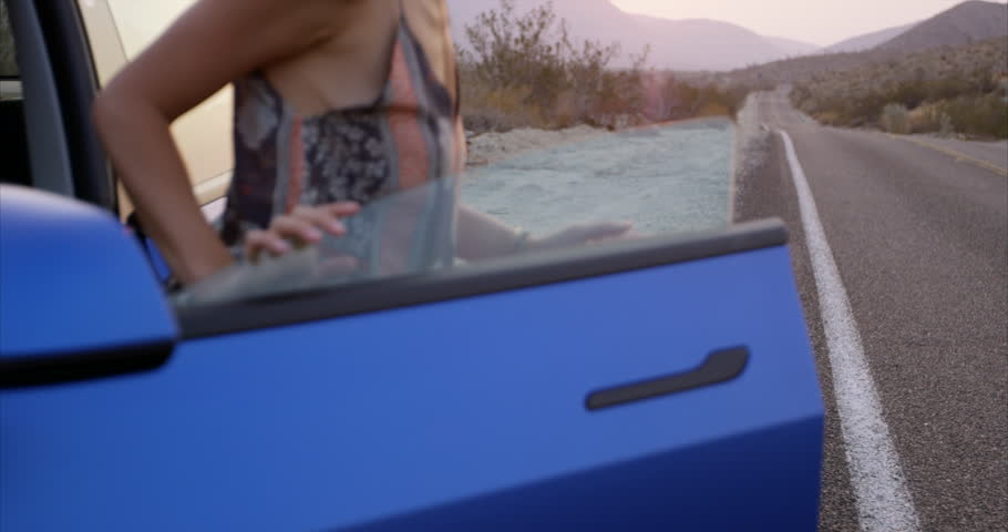 Young stylish woman gets out of blue on side of desert highway - rack focus