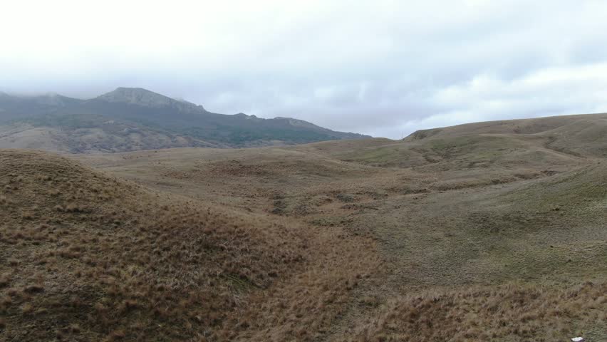 flight over the hills with dry grass on a cloudy day mountains