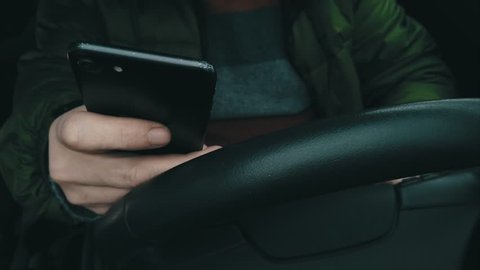A driver grasps and turns the steering wheel of a vehicle while driving with one hand, then takes out his smartphone to rest it on the steering wheel. Close-up, 4K.