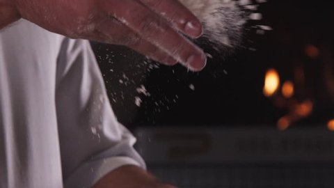 The hand is throwing flour. Someone making pizza. The chef is throwing flour on the table. Video of the food. The dough making process. White flour flies in the air.