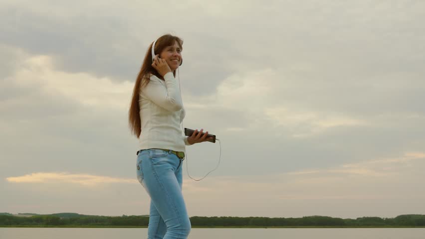 Happy woman walks on beach with tablet in spring and listens to music with headphones. beautiful girl in headphones walks on beach with tablet and is video conferencing online.