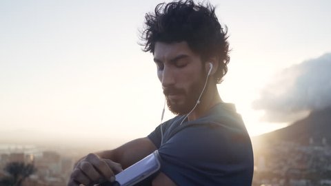 Young white brunette man in his workout clothes changing the music playing from his phone on his armband at sunrise