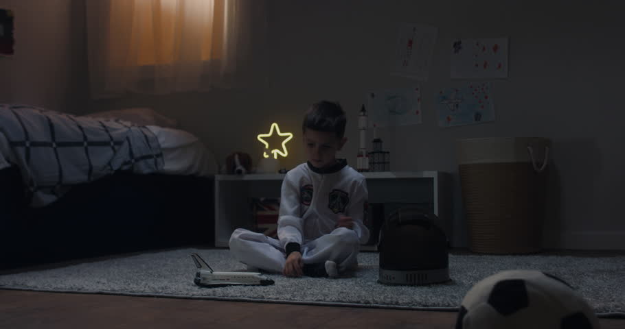 Cute little kid boy wearing astronaut suit playing with toy shuttle space ship rocket at home, bedroom interior evening shot. 4K UHD RAW FOOTAGE Royalty-Free Stock Footage #1026833012