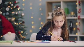 Portrait of cute little girl drawing with a yellow pencil then changing it on a blue one on Christmas tree lights background. Creativeness, talent, art class. Art therapy, holidays. Child?s portrait