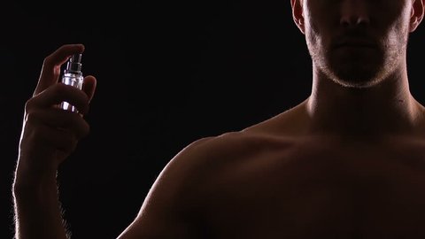 Athletic man spraying perfumes on torso, seductive fragrance for dating, slow-mo