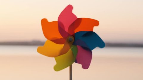 Plastic pinwheel rotate colored with blowing wind stands on sand by sea against the smooth surface of the sea and bright pink sunset. Toy mill on the beach. Large disk of the sun. Copy space. Relax