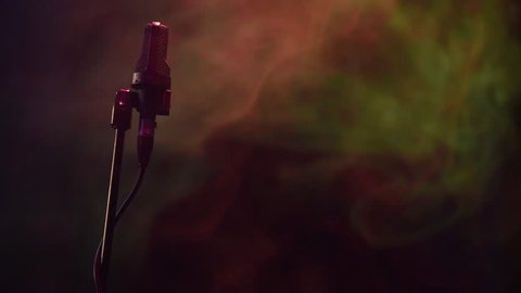 Low-key shot of microphone on a stand at a concert with colorful smoke in the background