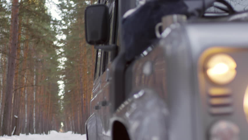 Tilt up of young Caucasian man with camera standing on car roof and taking pictures of trees