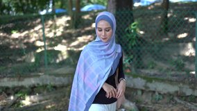Young woman in hijab walking around at green nature park, holding handbag, brand new Muslim women fashions.