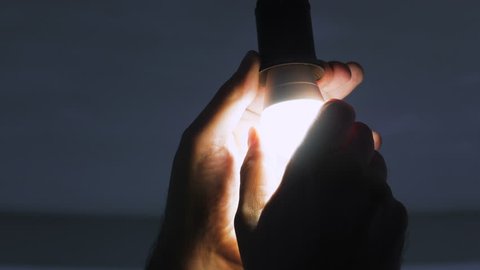 In a dark room, a man replaces an electric energy-saving lamp with a new LED lamp.