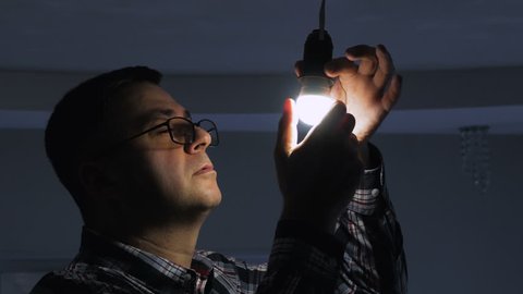 In a dark room, a man replaces an electric energy-saving lamp with a new LED lamp.