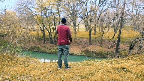 Man suffering from depression stands alone in woodland, watching river