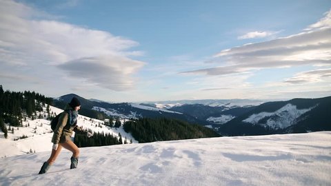 Young woman looking at the landscape while hiking in the winter mountains. Beautiful landscape with coniferous trees and white snow. Happy joyful woman having fun outdoors in winter enjoying beautiful