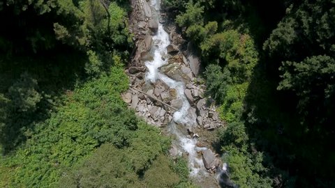 Aerial view of a mountain creek in the Alps at summer. Top down moving forward waterfall drone clip. Drone footage of a forest creek. Clear water in the forest.