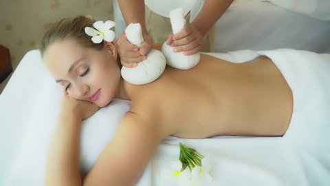 Beauty woman get warm herbal balls massage on back at spa shop, relieve stress and aids relaxation. Attractive beautiful girl get happy, smile. Charming beautiful woman lie prone on bed at spa salon.