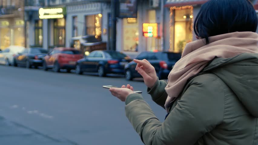 Unrecognizable woman standing on the street interacts HUD hologram with smartphone. Girl in warm clothes with a scarf uses technology of the future mobile screen on background of night city Royalty-Free Stock Footage #1026870647