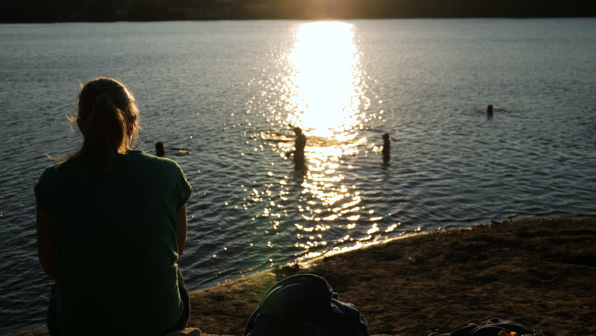 Static shot, of a mother watching kids playing in the water, at sunset, at a south Norwegian lake, on a sunny, summer evening, in Norway