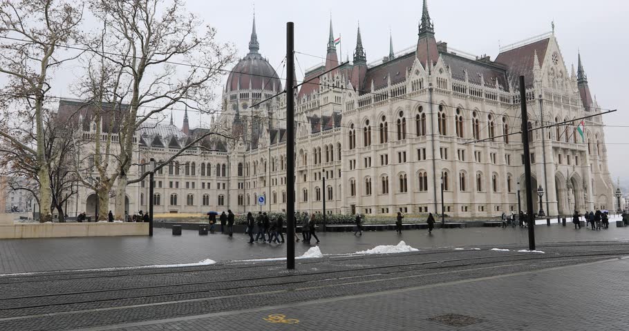 BUDAPEST, HUNGARY - JANUARY 16, 2019 : Yellow tram passes in front of the Gothic architecture of famous Hungarian Parliament building exterior view at winter time | Shutterstock HD Video #1026875042