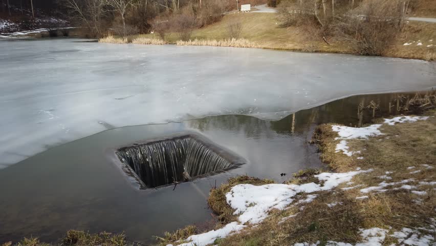Ice covered pond with overflow water running off.