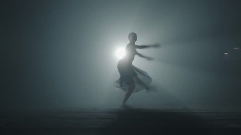 Diligent young graceful ballerina dancing elements of classical ballet in the dark with light and smoke on the background. Beautiful young ballerina in darkness. Ballet practice in studio.