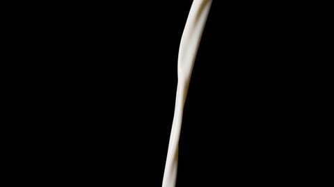 Macro shot of pouring milk in slow motion in front of black background.