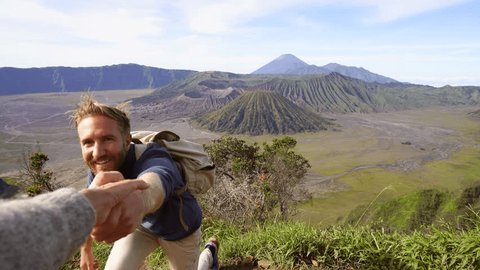 Helping concept: Couple hiking on volcanic landscape in Indonesia. Hand reach out to help male hiker reach the top. Hiking helping hand concept 