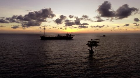 Aerial view Silhouette of oil production platform or oil rig with supply vessel during sunset at oil field 