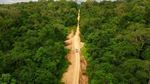 A pick up truck drives along a dirt trail in the Amazon Rainforest. Aerial shot.